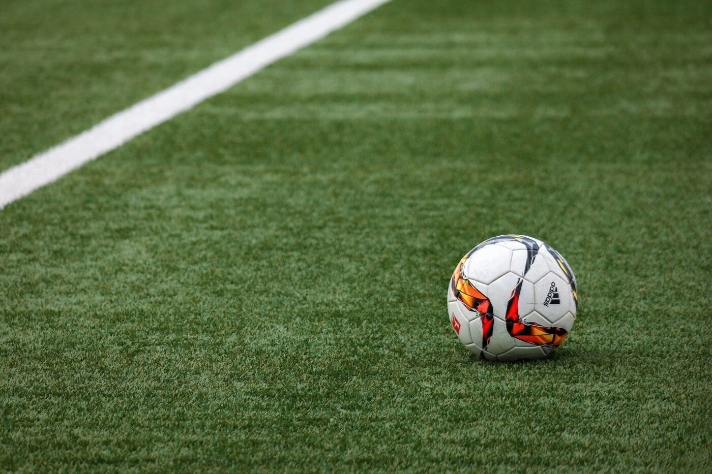 A soccer ball with colorful patterns rests on a neatly trimmed green field near a white boundary line. The field, showcasing synthetic grass solutions, appears well-maintained under natural light, echoing the meticulous artificial turf installations often seen in Gilbert AZ.